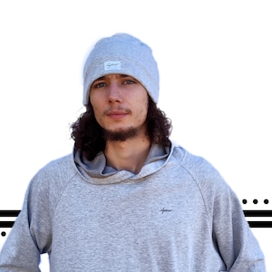 Può includere: Una persona che indossa una felpa con cappuccio grigia con un piccolo logo sul davanti e un berretto di lana grigio con un logo sul davanti.
