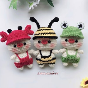 May include: Three crocheted stuffed animals: a red crab, a yellow and black bee, and a green frog. Each animal is wearing a crocheted outfit and has a smiling face.