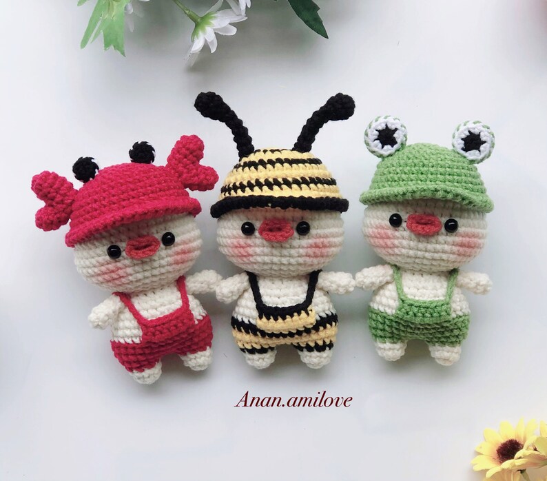 May include: Three crocheted stuffed animals: a red crab, a yellow and black bee, and a green frog. Each animal is wearing a crocheted outfit and has a smiling face.