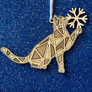 May include: A wooden Christmas ornament shaped like a cat holding a snowflake. The cat is made of geometric shapes and has a brown wood finish.