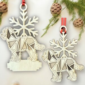 May include: Two wooden Christmas ornaments shaped like dogs with geometric patterns. The ornaments are hanging from red ribbon and have a snowflake design behind them.