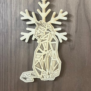 May include: A wooden Christmas ornament shaped like a cat with a snowflake design. The cat is made of geometric shapes and is outlined in black.