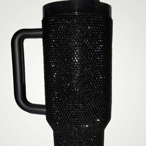 Puede incluir: Una taza de viaje negra con asa y tapa. La taza est&aacute; cubierta de diamantes de imitaci&oacute;n negros.