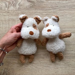 May include: Two handmade plush dog toys. Each dog has a white body with brown accents on the ears, paws, and spots. The toys are held together, suggesting a pair or set. The plushies are soft and cuddly, perfect for children or as decorative items.