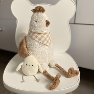 May include: A white plush chicken with brown accents, wearing a tan and white checkered scarf, and a smaller chick toy. The chicken is seated on a white chair with a unique bear-shaped back.