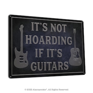 May include: A black metal sign with a distressed finish. The sign features a silver silhouette of an electric guitar and an acoustic guitar. The text on the sign reads "It's not hoarding if it's guitars."