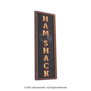 May include: A rustic metal sign with the words "HAMSHACK" in vertical, raised, wooden letters on a black background. The sign has a brown wooden frame.