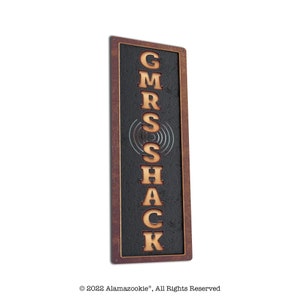May include: A rustic metal sign with a black background and a brown wooden frame. The sign says "GMRS Shack" in gold letters.