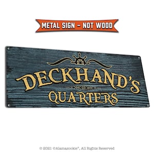 May include: A blue and gold metal sign with the text "Deckhand's Quarters" and a nautical wheel design. The sign has a wood grain texture.