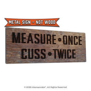 May include: A rustic metal sign with a woodgrain texture. The sign reads "MEASURE ONCE CUSS TWICE" in black lettering. The sign has a red banner at the top that reads "METAL SIGN - NOT WOOD".