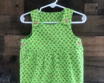 May include: A green and pink floral print baby overall with pink buttons. The overall has a gathered waist and is made of a soft, lightweight fabric.