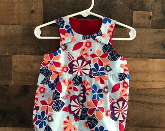 May include: A blue and white floral print baby romper with a red collar. The romper has a gathered waist and a ruffled hem.