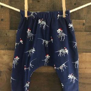 May include: Blue baby pants with a Christmas dinosaur skeleton print. The pants have red and white striped cuffs.