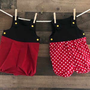 May include: Two red and black baby onesies with yellow buttons. One onesie has white polka dots.