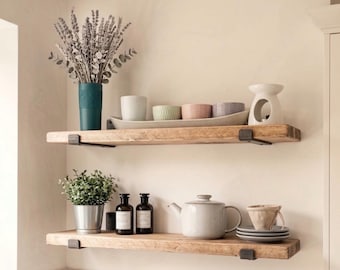 Puede incluir: Dos estantes de madera rústica montados en la pared, con un jarrón azul verdoso con lavanda seca, una bandeja de cerámica con cuencos pequeños, un quemador de aceite blanco, una planta verde, dos botellas de vidrio oscuro, una tetera y platillos.