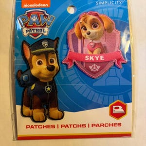 May include: A package of Nickelodeon Paw Patrol iron-on patches. The package features two patches: Chase in a police uniform and Skye in a pink outfit. The package has the Paw Patrol logo and the word "SIMPLICITY". The bottom of the package reads "PATCHES".