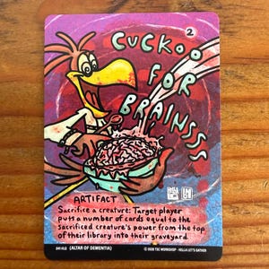May include: A trading card with a cartoon bird character and the text "Cuckoo for Brains." The card features a colorful design with a brain graphic and the word "Artifact." The card's text describes a game mechanic.