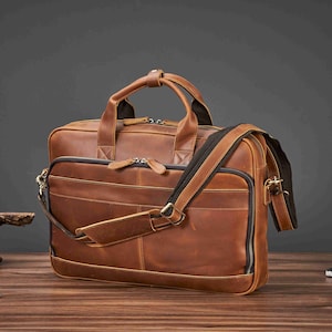 May include: A brown leather briefcase with a top handle and a detachable shoulder strap. The bag has multiple zippered compartments and a classic, professional design. The leather has a distressed finish.