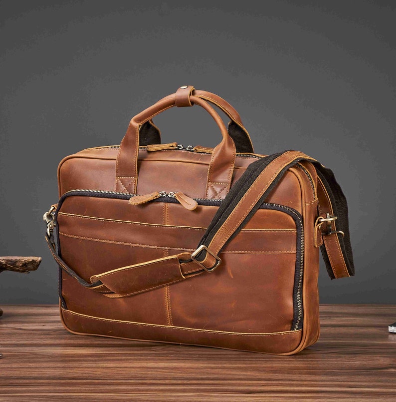 May include: A brown leather briefcase with a top handle and a detachable shoulder strap. The bag has multiple zippered compartments and a classic, professional design. The leather has a distressed finish.