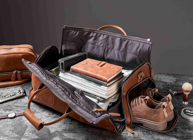 May include: Open brown leather travel bag with a variety of items inside, including a speaker, books, and a pair of brown shoes. A smaller brown leather bag is visible in the background.