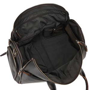 May include: Open view of a dark brown leather travel bag with multiple compartments and zippers. The bag has a large main compartment and several smaller pockets for organization. The interior is lined with a dark fabric.