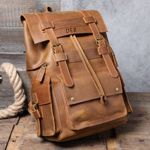 May include: A brown leather rucksack with a large front pocket and multiple buckles. The rucksack has a personalised name, "DEB", on the front.