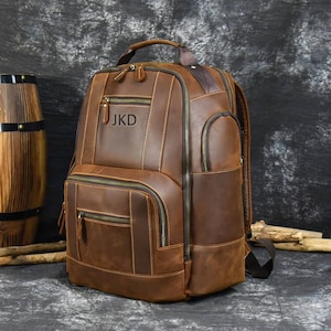 May include: A brown leather backpack with multiple pockets and a zipper closure. The backpack has the initials "JKD" embossed on the front.