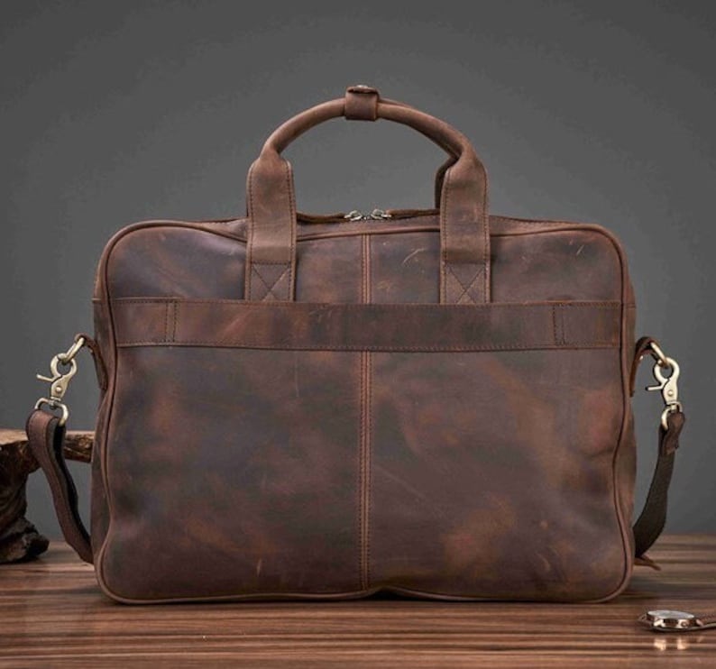 May include: A brown leather briefcase with a top handle and a detachable shoulder strap. The bag has a rectangular shape with a front pocket and metal hardware. The leather has a distressed finish.