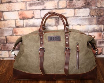 Pode incluir: Uma bolsa de viagem de lona verde com detalhes e alças de couro marrom. A bolsa tem um bolso com zíper na frente e um remendo de couro personalizado com as iniciais "RCF".