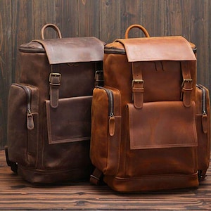 May include: Two leather backpacks, one brown and one tan, with adjustable straps and multiple pockets.