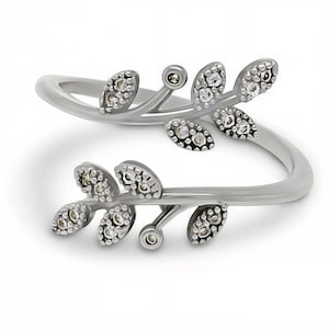 May include: A silver-toned bypass ring featuring two overlapping branches with textured leaves. Each leaf is accented with small, clear, sparkling stones embedded within the metal, creating a delicate, nature-inspired design.