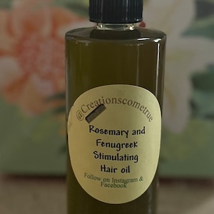 May include: A dark green glass bottle with a black cap and a white label that reads "Rosemary and Fenugreek Stimulating Hair oil Follow on Instagram & Facebook @Creationscometrue".
