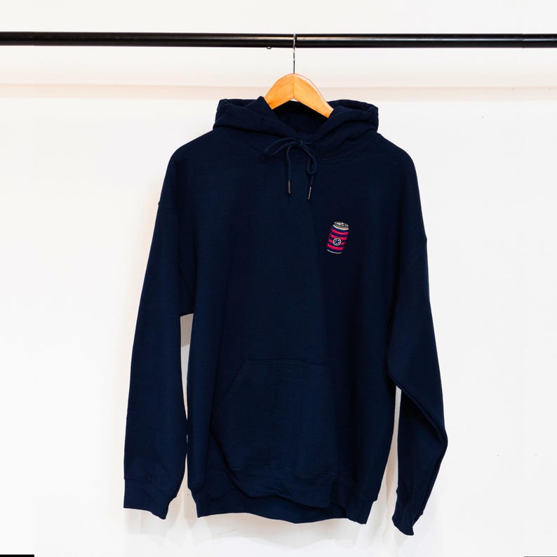 May include: A navy blue hoodie with a small embroidered image of a can on the front. The hoodie has a drawstring hood and a kangaroo pocket.
