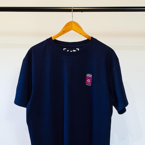 K&ouml;nnte beinhalten: Ein marineblaues T-Shirt mit einem kleinen, rosa-wei&szlig; gestreiften Dosenmotiv auf der Vorderseite.