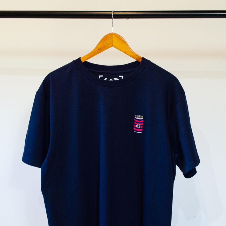 K&ouml;nnte beinhalten: Ein marineblaues T-Shirt mit einem kleinen, rosa-wei&szlig; gestreiften Dosenmotiv auf der Vorderseite.