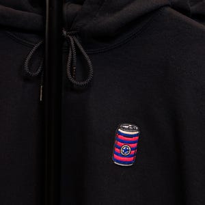 May include: Black hoodie with a red, white, and blue striped can with a star on it.