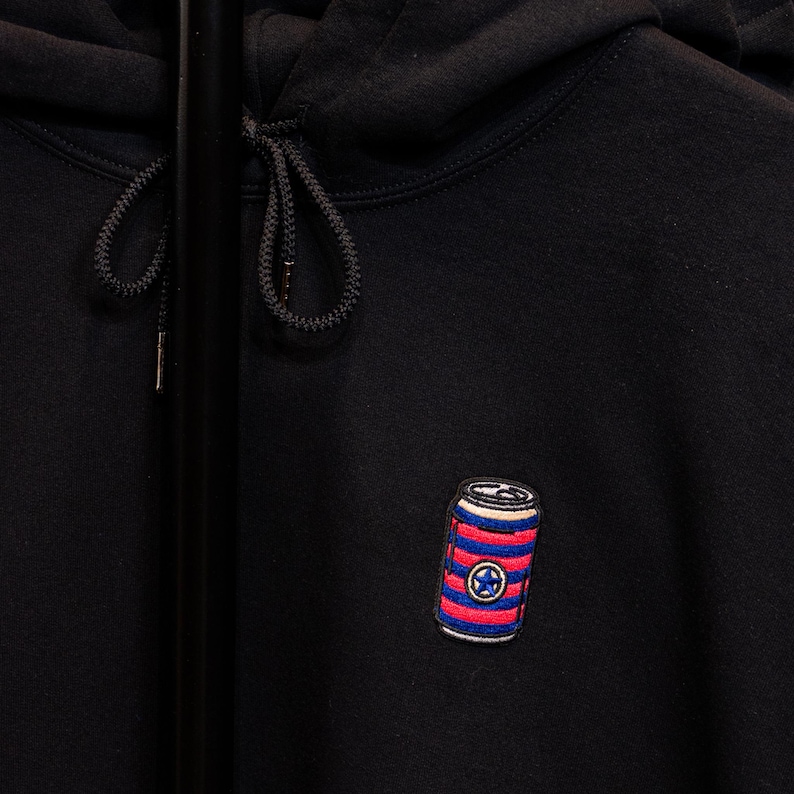 May include: Black hoodie with a red, white, and blue striped can with a star on it.