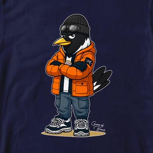 Puede incluir: Camiseta azul marino con un personaje de caricatura de urraca que lleva una chaqueta acolchada naranja, un gorro negro y gafas de aviador. La urraca tambi&eacute;n lleva vaqueros azules y zapatillas deportivas. El texto "Game of Brews" est&aacute; en la parte inferior derecha.