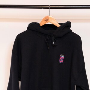 May include: Black hooded sweatshirt with a small embroidered image of a red, white, and blue striped can on the left chest.