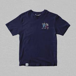 May include: Navy blue t-shirt featuring a small graphic of two cartoon figures. One figure is blue and the other is purple. The shirt has a small tag at the bottom left and a small logo at the top.