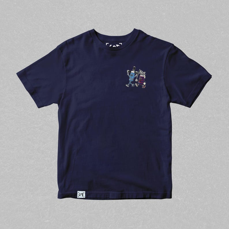 May include: Navy blue t-shirt featuring a small graphic of two cartoon figures. One figure is blue and the other is purple. The shirt has a small tag at the bottom left and a small logo at the top.