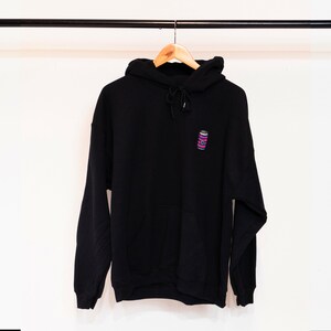May include: Black hooded sweatshirt with a small embroidered design of a pink and blue striped can on the front.