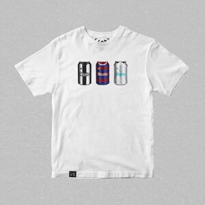 K&ouml;nnte beinhalten: Wei&szlig;es T-Shirt mit einem Aufdruck von drei Aluminiumdosen. Jede Dose zeigt das Trikotdesign eines anderen Fu&szlig;ballteams. Die Trikots sind schwarz-wei&szlig;, rot-blau und wei&szlig;-blau.