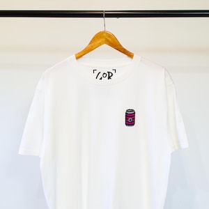 K&ouml;nnte beinhalten: Wei&szlig;es T-Shirt mit einem Design einer rosa-schwarzen gestreiften Dose und dem Text "[COR]" auf der Vorderseite.
