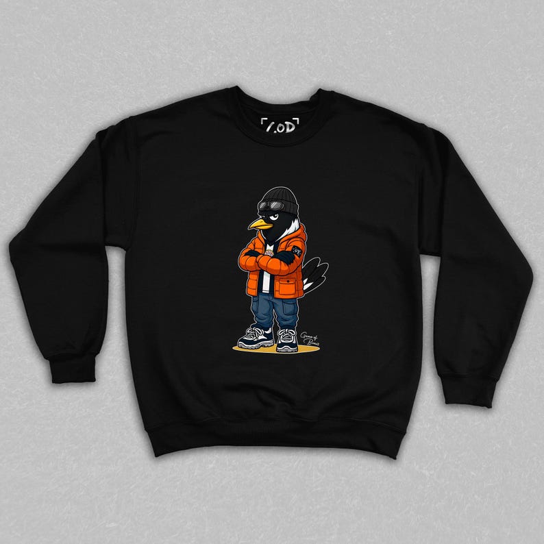 May include: Black crewneck sweatshirt featuring a cartoon crow character wearing a black beanie, orange jacket, blue jeans, and sneakers. The crow has its arms crossed and is wearing sunglasses. The sweatshirt has the text "/.OD" printed on the top.