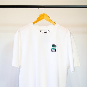 May include: White t-shirt with a small embroidered image of a green and white can on the front. The text "[can]" is printed on the neck.