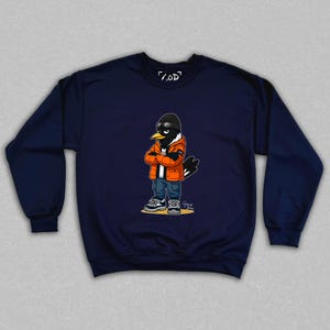 May include: Navy blue sweatshirt featuring a cartoon raven character wearing an orange jacket, black beanie, and jeans. The raven has its arms crossed and is wearing sunglasses. The sweatshirt has the text "/.OD" on the top.