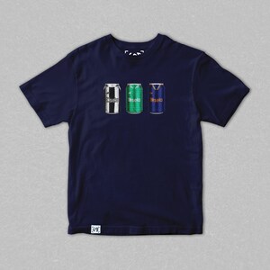 May include: Navy blue t-shirt featuring three stylized beverage cans. The cans are decorated with team colors and logos. The text "fasela" is printed on each can. The shirt has a crew neck and short sleeves.