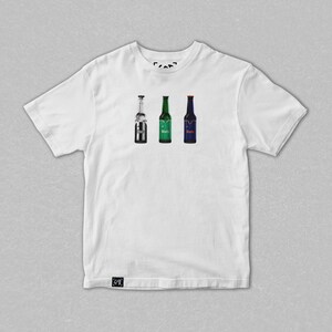 May include: White t-shirt featuring three beer bottle illustrations. The bottles are in silver, green, and blue, each with a different label. The shirt has a crew neck and short sleeves. The shirt is made of a soft, comfortable material.