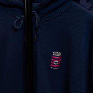 May include: A navy blue hoodie with a red, white, and blue striped can with a star on it embroidered on the front.